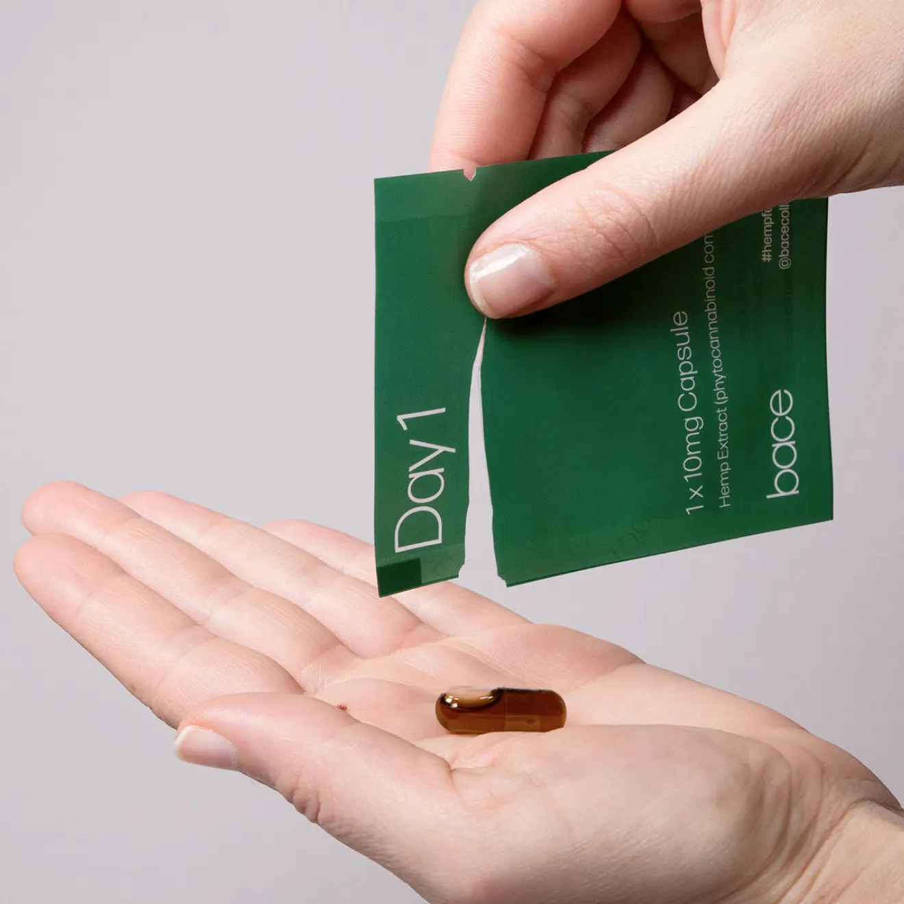 A Day 1 dosage packet torn open over an open palm, revealing a single capsule