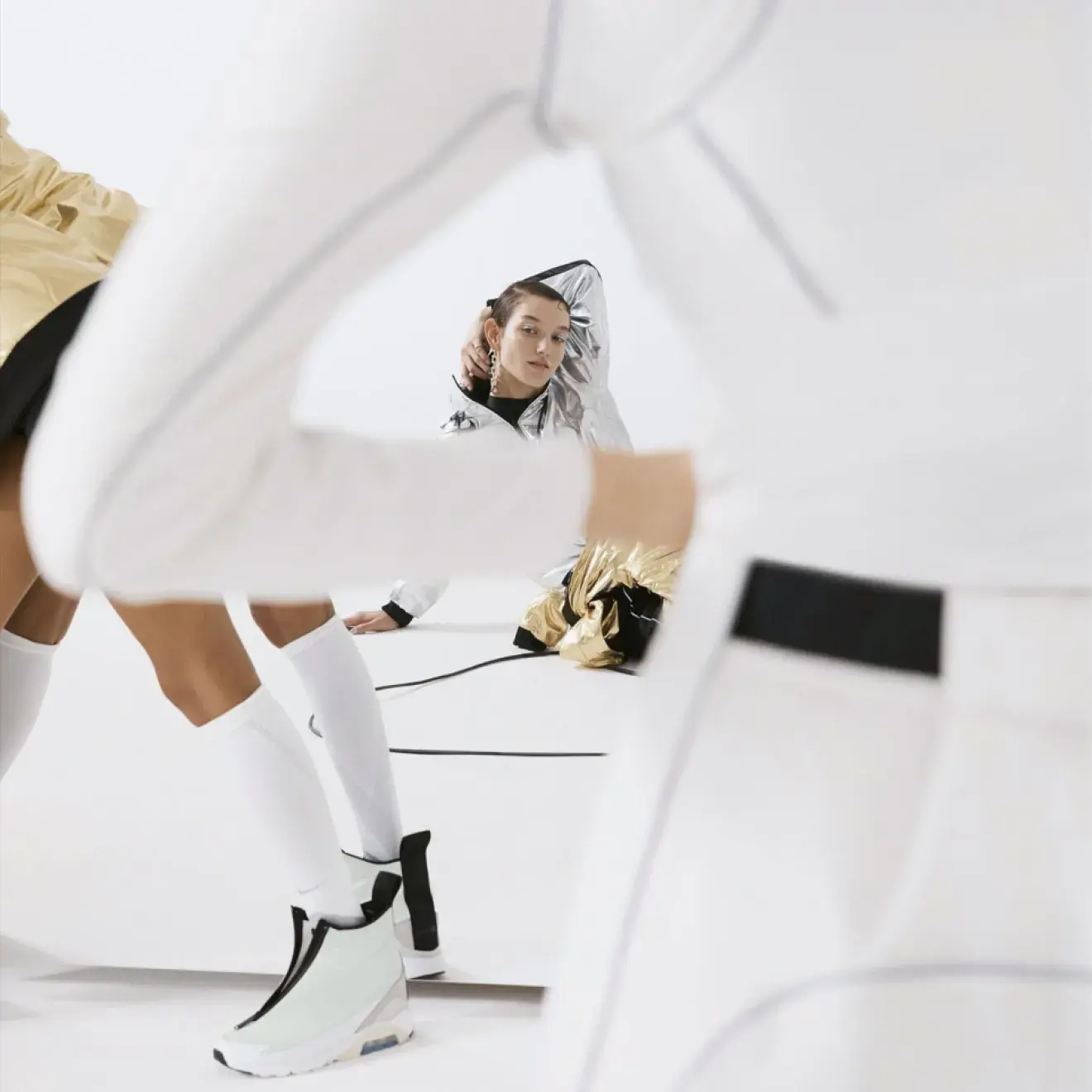 Campaign photography of a model in metallic outerwear, shot through an abstract foreground